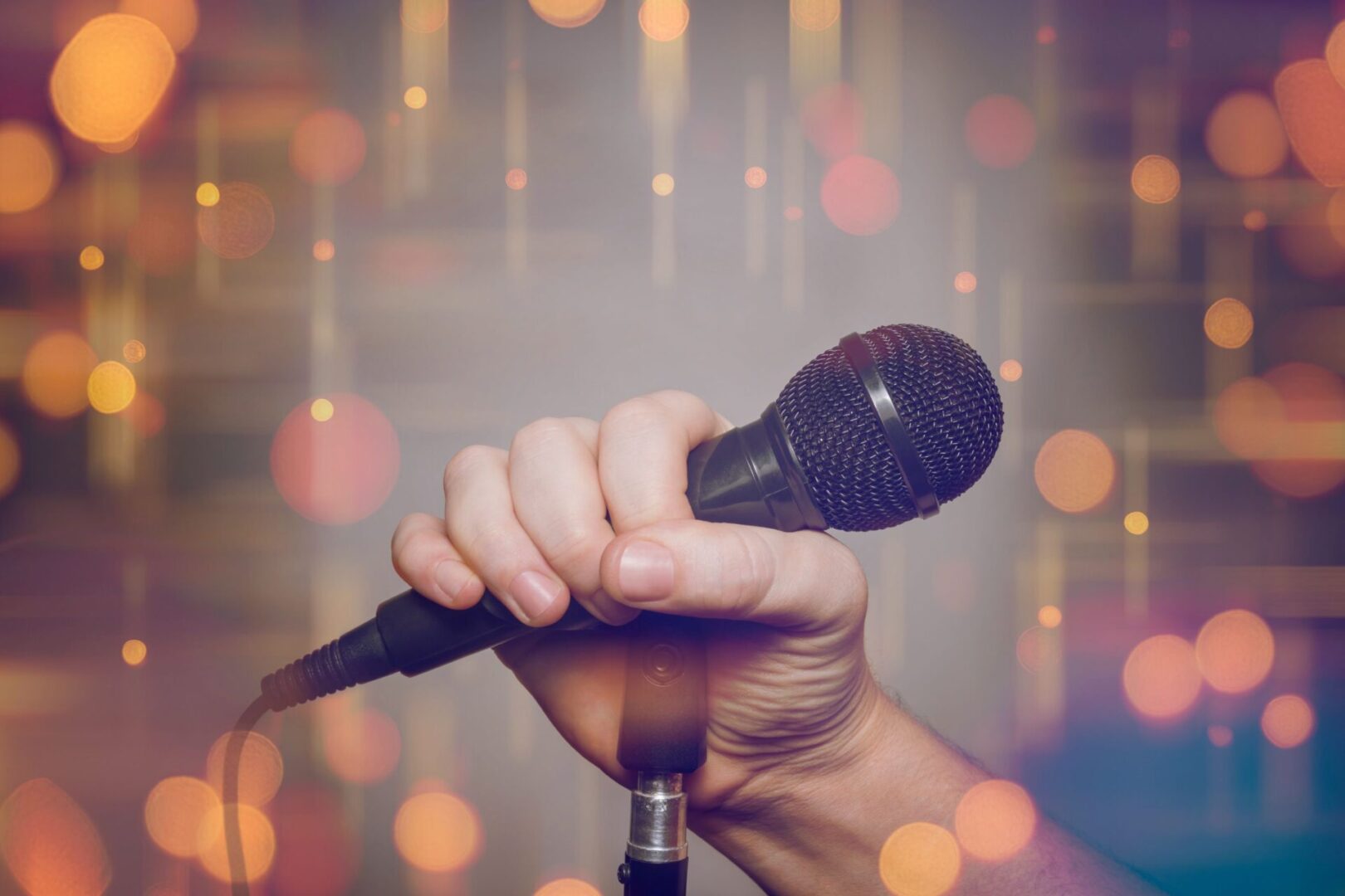 Hand holding microphone with bokeh lights.
