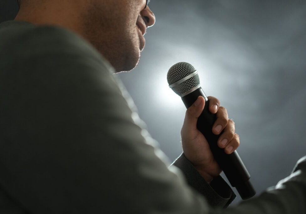 Person holding microphone, speaking on stage.
